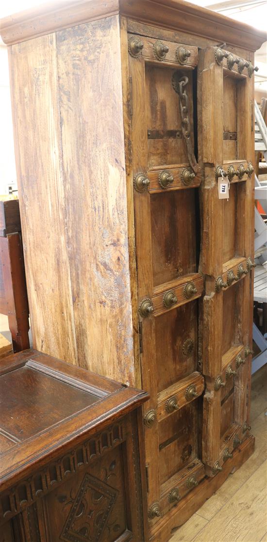 An Indian hardwood narrow cupboard, fitted panelled doors decorated with brass bosses and chain fastening, H.178cm